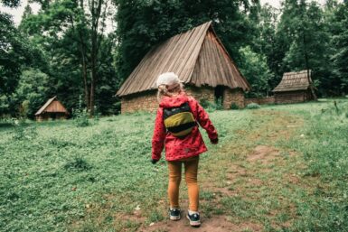 a girl in a red jacket is walking towards a hut